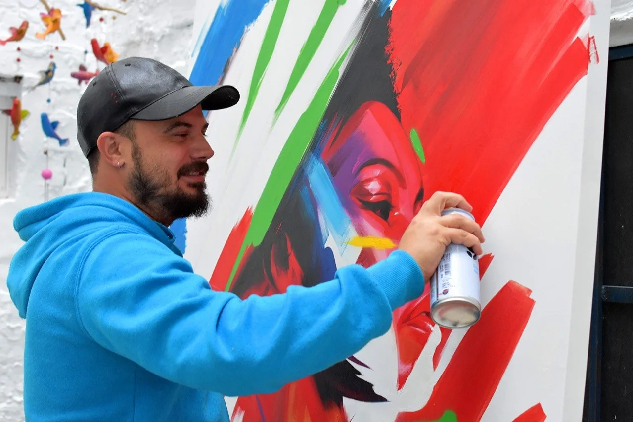 Manomatic pintando. Manomatic es un artista grafitero pionero del arte urbano en Huelva especializado en artes visuales y diseño gráfico. Su obra trata en especial temáticas sociales enmarcadas en imágenes de hiperrealismo conceptual. «God save the queer» se realizó para el Festival Serpis Urban Project (Valencia), 2018. Técnica: graffiti.